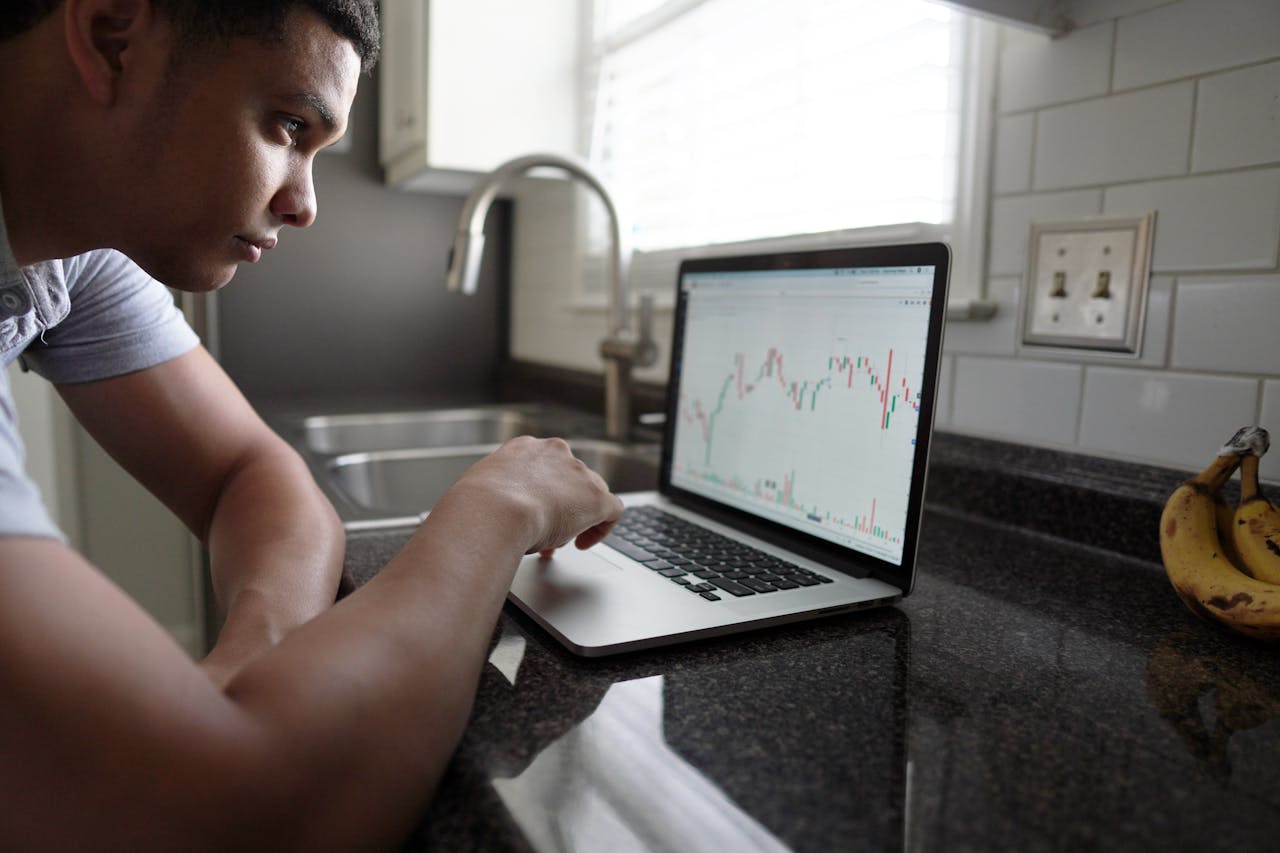 journey-img Focused man examining financial graphs on a laptop in a modern kitchen setting.
